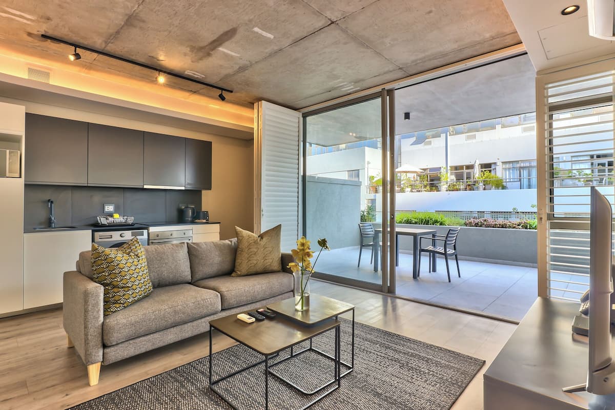 Un salon moderne avec un canapé, une table basse et une vue sur un balcon aménagé avec du mobilier d’extérieur.
