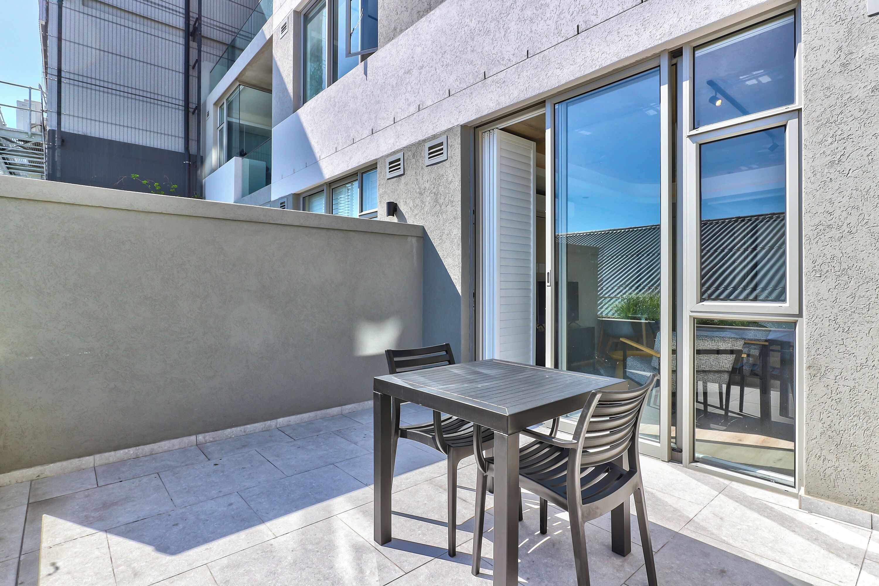Un patio exterior con una mesa y sillas, una puerta corrediza de vidrio y vista a la calle.