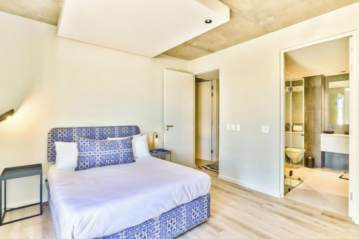 A modern bedroom with a large bed, bedside tables, and a bathroom visible through an open door.