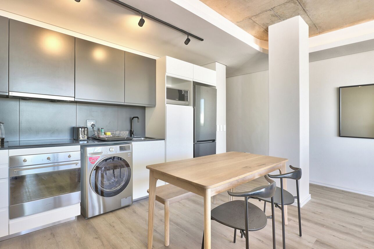 A modern kitchen with stainless steel appliances, a wooden table, and two chairs.