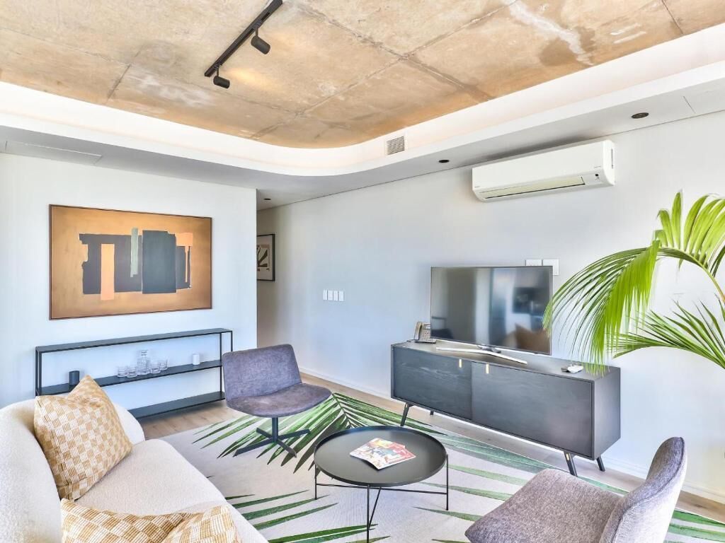 Un salon moderne comprenant un canapé, des fauteuils, une table basse, un téléviseur et un grand tableau.