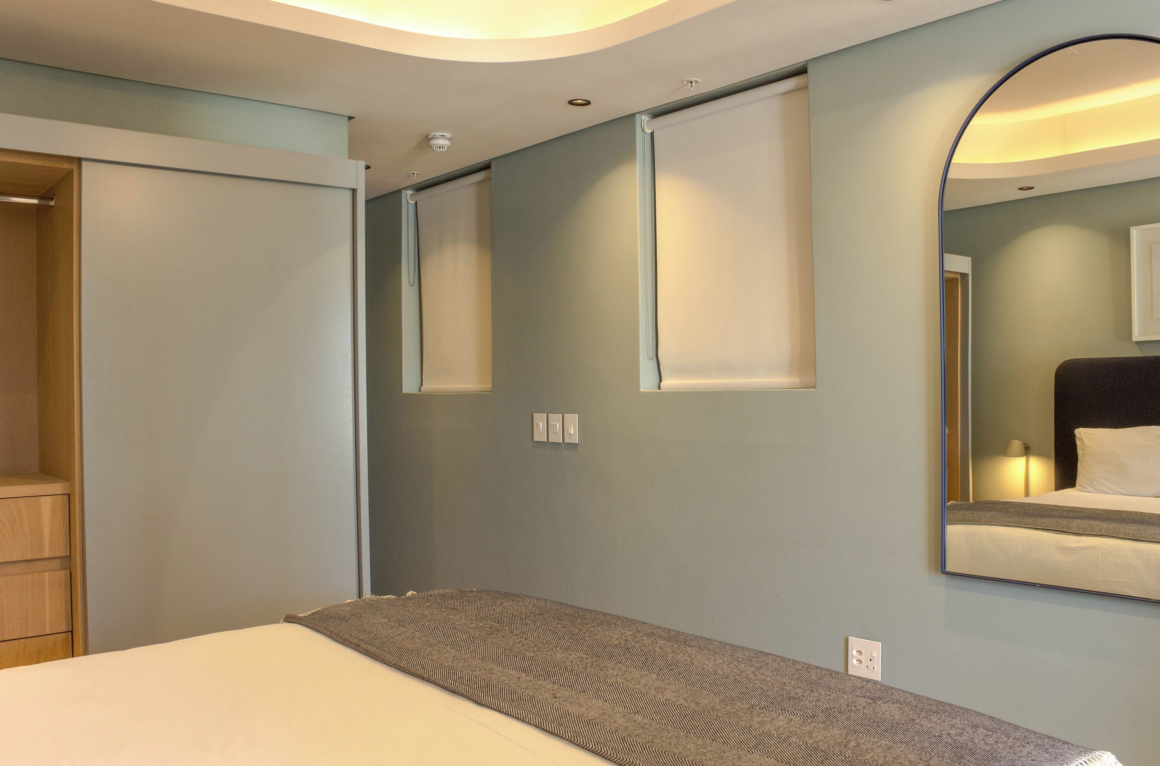 A modern hotel room with a large bed, a wardrobe, a mirror, and a ceiling light.