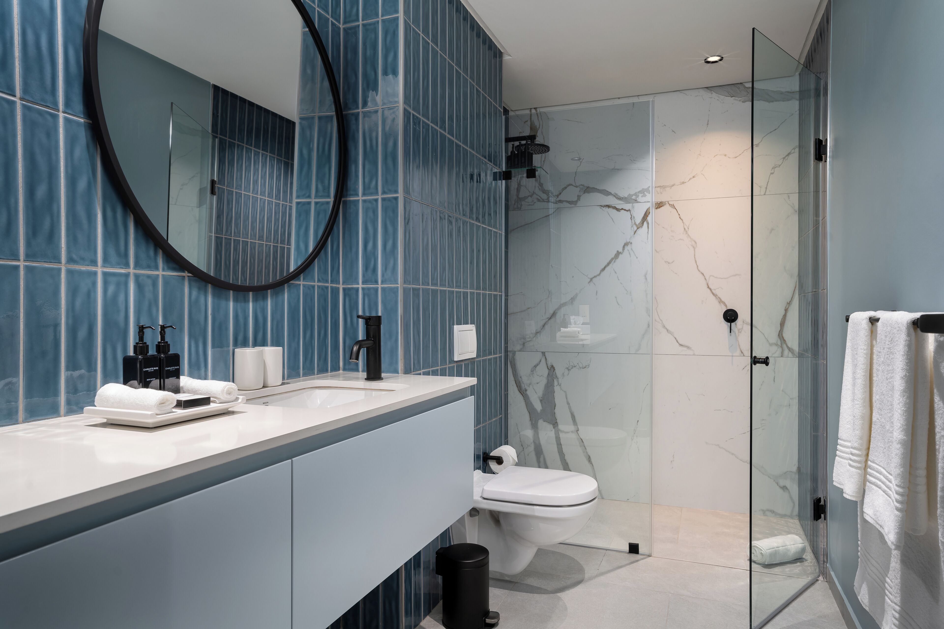 A modern bathroom with a glass shower enclosure, a white toilet, and a vanity with a mirror and sink.