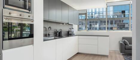 Uma cozinha moderna com eletrodomésticos embutidos, uma janela grande e um sofá cinzento.