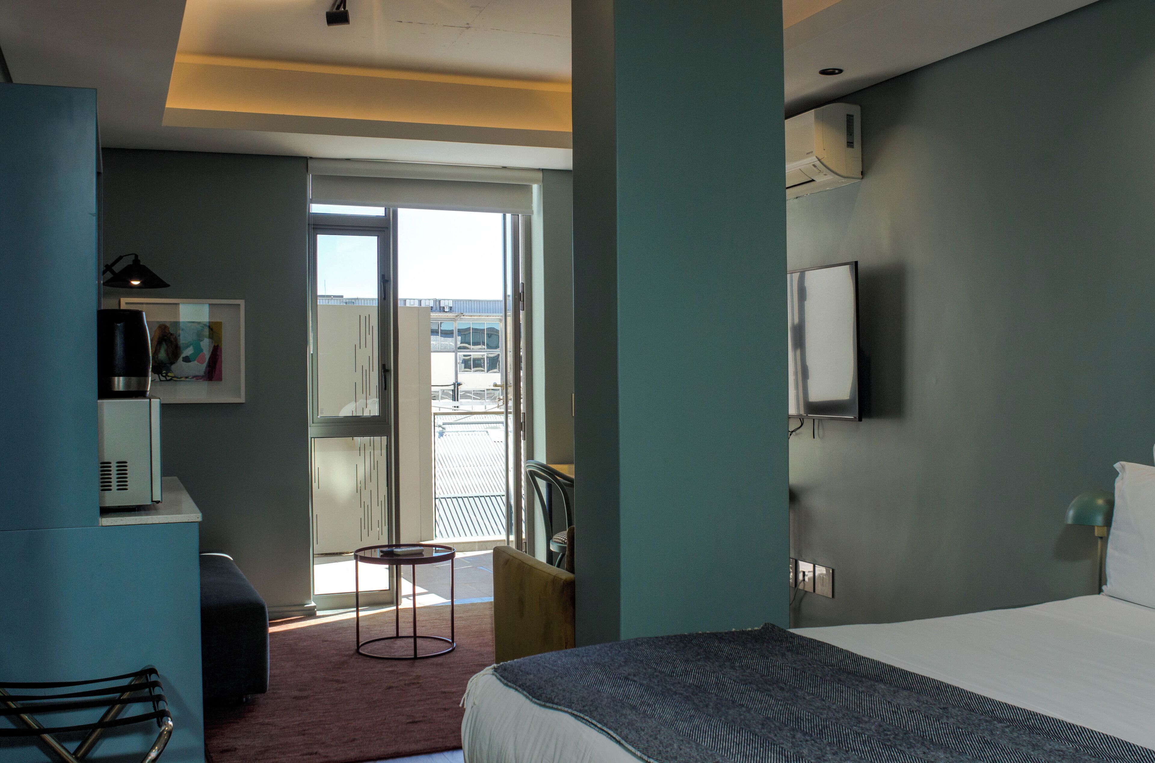 A hotel room with a bed, a desk, a chair, a small table, and a view of the outside.