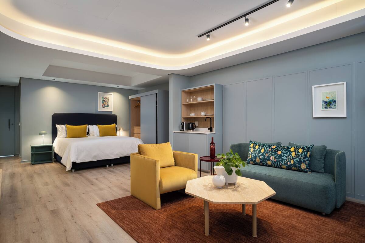 Une chambre à coucher moderne avec un lit, un fauteuil jaune, un canapé vert et une table basse.