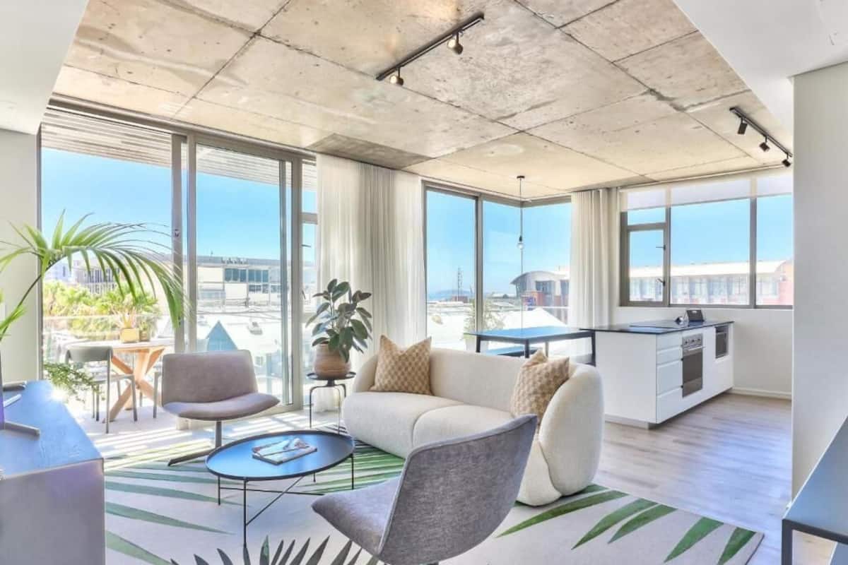 Un appartement moderne comprenant un espace de vie, une cuisine et de grandes fenêtres offrant une vue sur la ville.