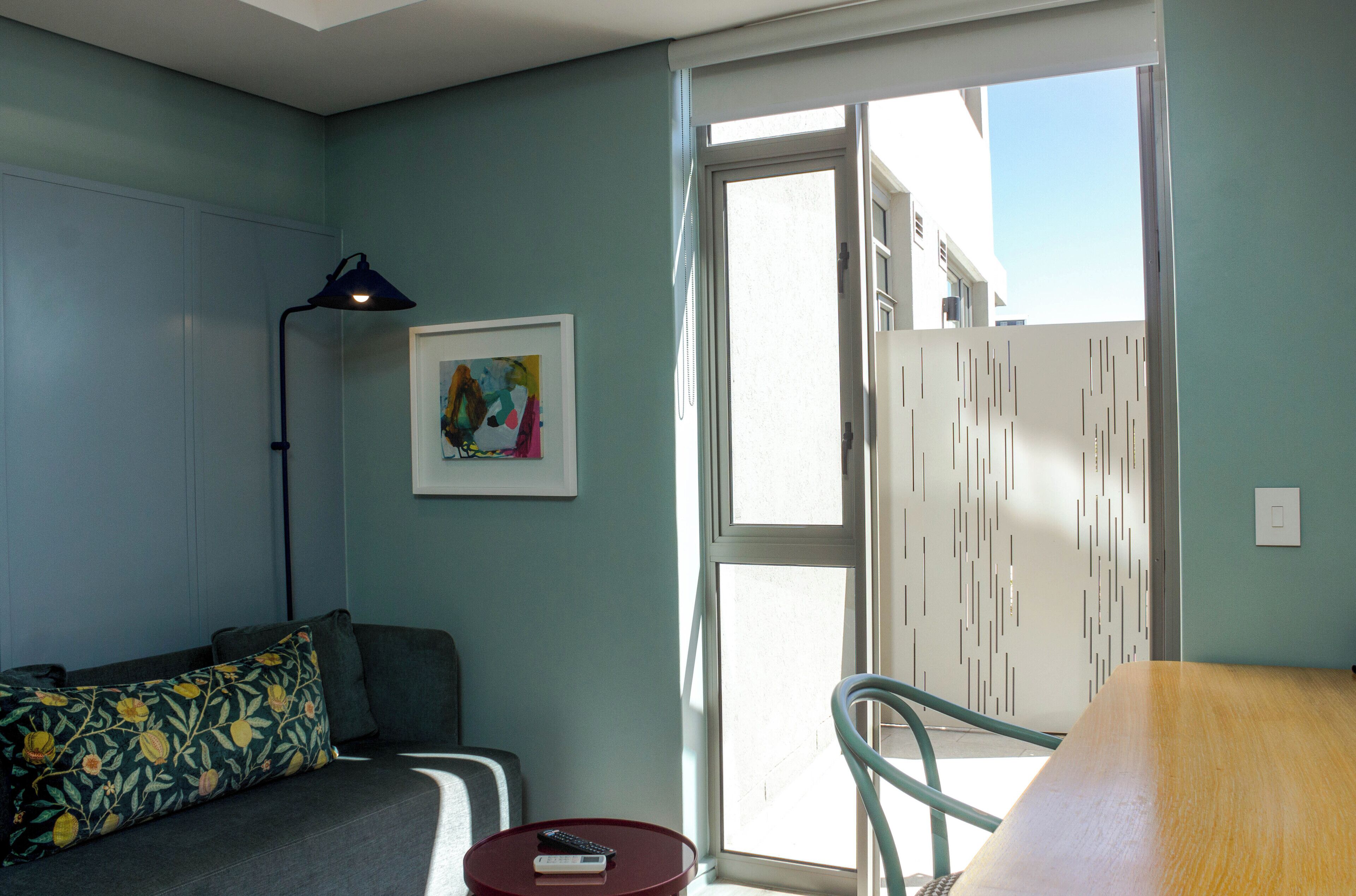 Una sala de estar con un sofá, una mesa y una silla. Hay un cuadro en la pared y una lámpara en una mesita.