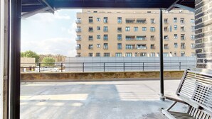 Une vue depuis un balcon donnant sur un immeuble à plusieurs étages, lui-même doté de balcons, ainsi que sur un parking et un mur de pierre.