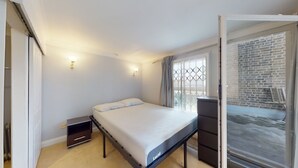 Une chambre à coucher comprenant un lit, des tables de chevet, une armoire et une porte-fenêtre coulissante donnant sur un balcon avec un mur en briques.