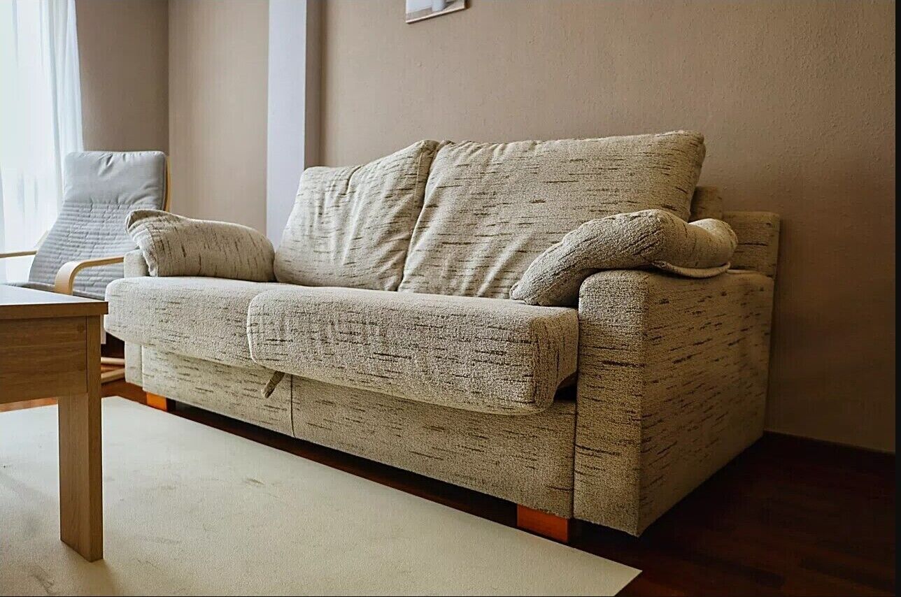 En beige soffa med ett mönstrat tyg, ett soffbord i trä och en stol med en kudde.