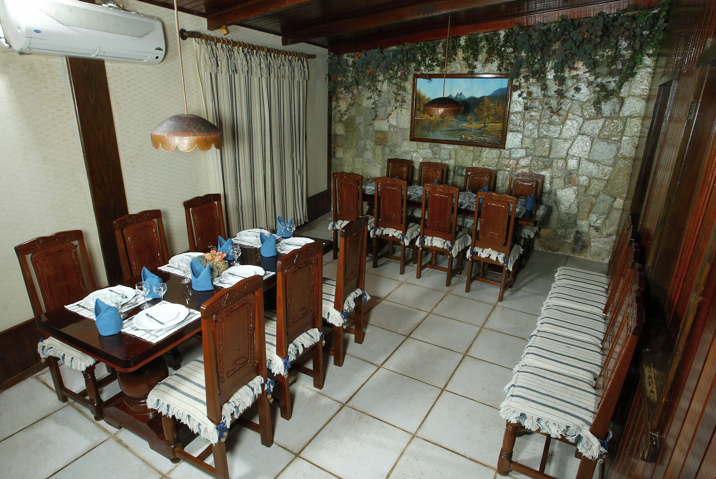 Uma sala de jantar com parede de pedra, cadeiras de madeira, mesa posta para seis e um banco.