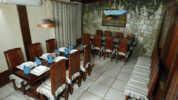 Uma sala de jantar com parede de pedra, cadeiras de madeira, mesa posta para seis e um banco.