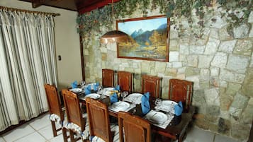 A dining area with a stone wall, wooden chairs, a table set for six, and a painting above the table.