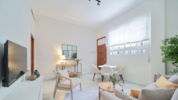 A modern living room with a flat-screen TV, a dining area with a table and chairs, and a large window with a view.