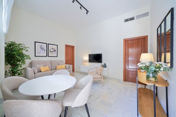 A modern living room with a sofa, a dining table, and chairs. There is a TV mounted on the wall, a plant, and a lamp on a side table. - iloftmalaga Carreteria 77 - II (Malaga)