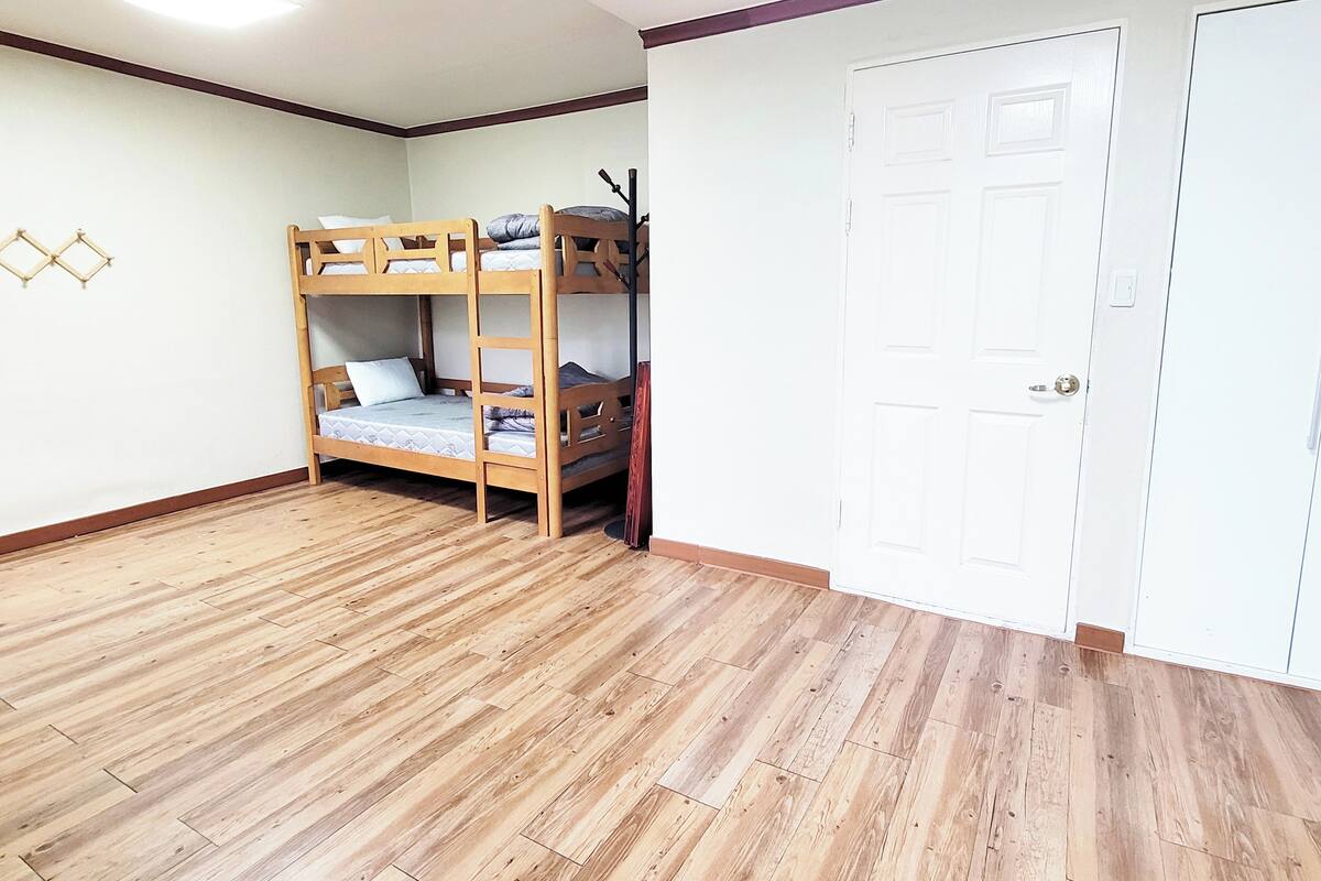 A room with a bunk bed, wooden flooring, a white door, and a wall-mounted light fixture.