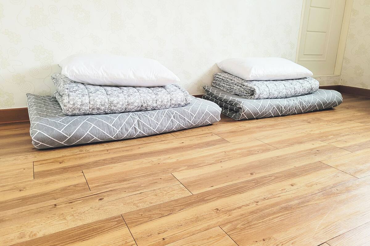 Two bedside tables with pillows and folded blankets, wooden flooring, and a white door in the background.