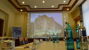 A conference room with a projection screen displaying a hotel image, a long table with chairs, and several bottles of water.