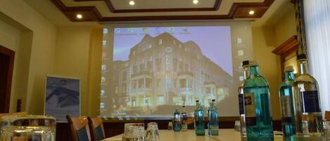A conference room with a projection screen displaying a hotel image, a long table with chairs, and several bottles of water.