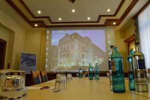 Ein Konferenzraum mit einer Projektionsleinwand, die ein Hotel zeigt, einem langen Tisch mit Stühlen und mehreren Wasserflaschen.