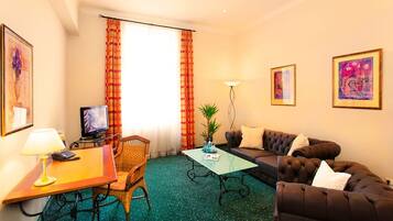 A hotel room with a television, a desk with a lamp, a sofa, a coffee table, and a large window with curtains.