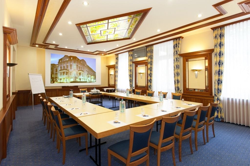 Uma sala de conferência com uma mesa comprida, cadeiras, uma tela de projetor e um quadro branco.