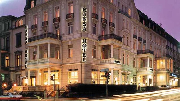 Il s'agit d'un bâtiment historique dont l'inscription « Hansa Hotel » est bien visible. Il présente un style architectural classique, avec de nombreux balcons et de grandes fenêtres.