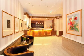 Eine Hotelhalle mit einer Rezeption, gerahmten Kunstwerken an den Wänden und Sitzbereichen.