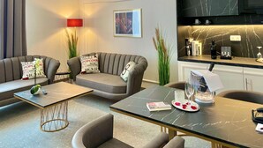 Un salon moderne avec deux canapés, une table basse et une table à manger. Un téléviseur est fixé au mur, ainsi qu’une lampe et un tableau encadré.