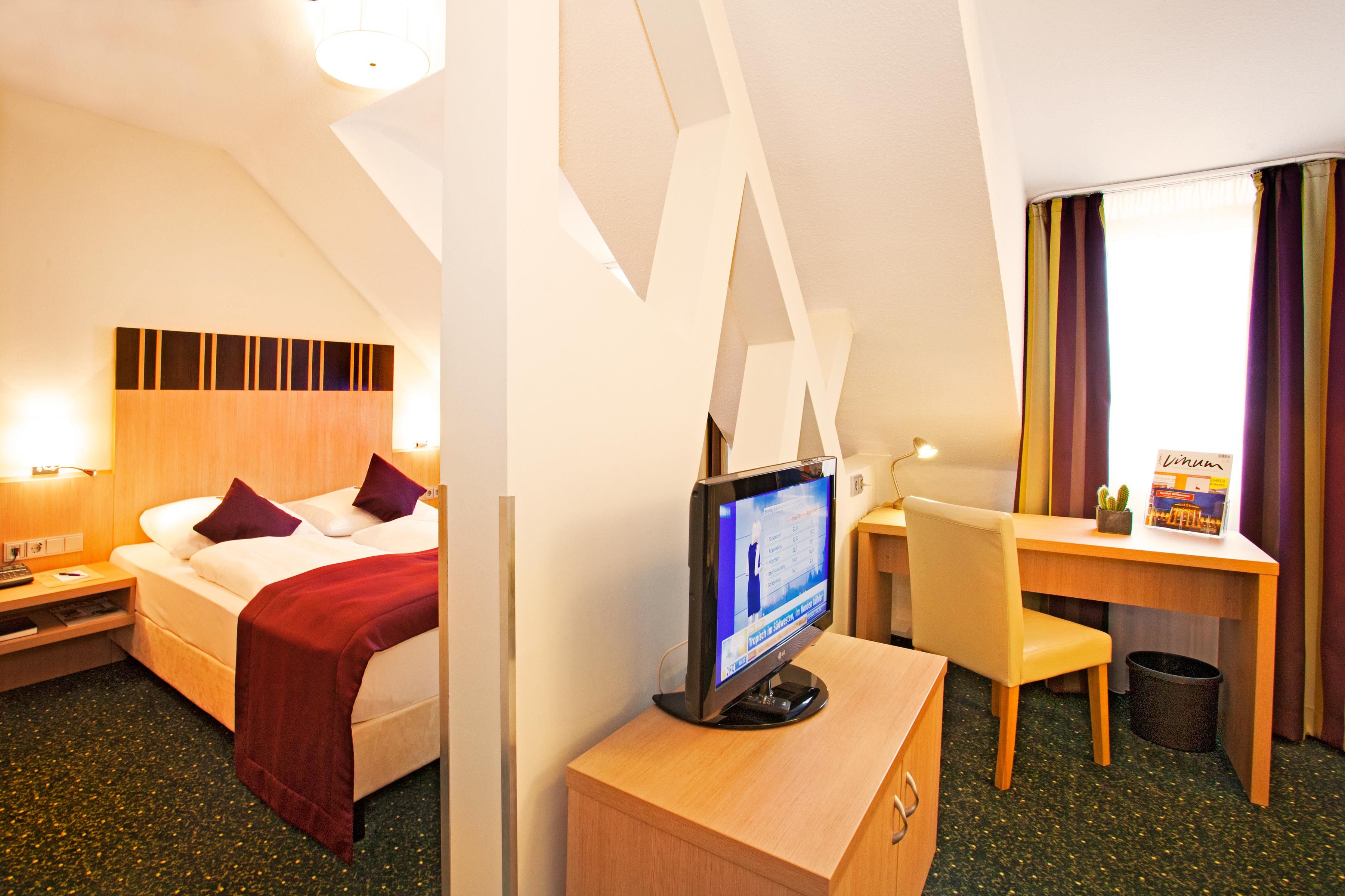 Ein Hotelzimmer mit einem Bett, einem Schreibtisch, einem Fernseher und einem Fenster mit Vorhängen.
