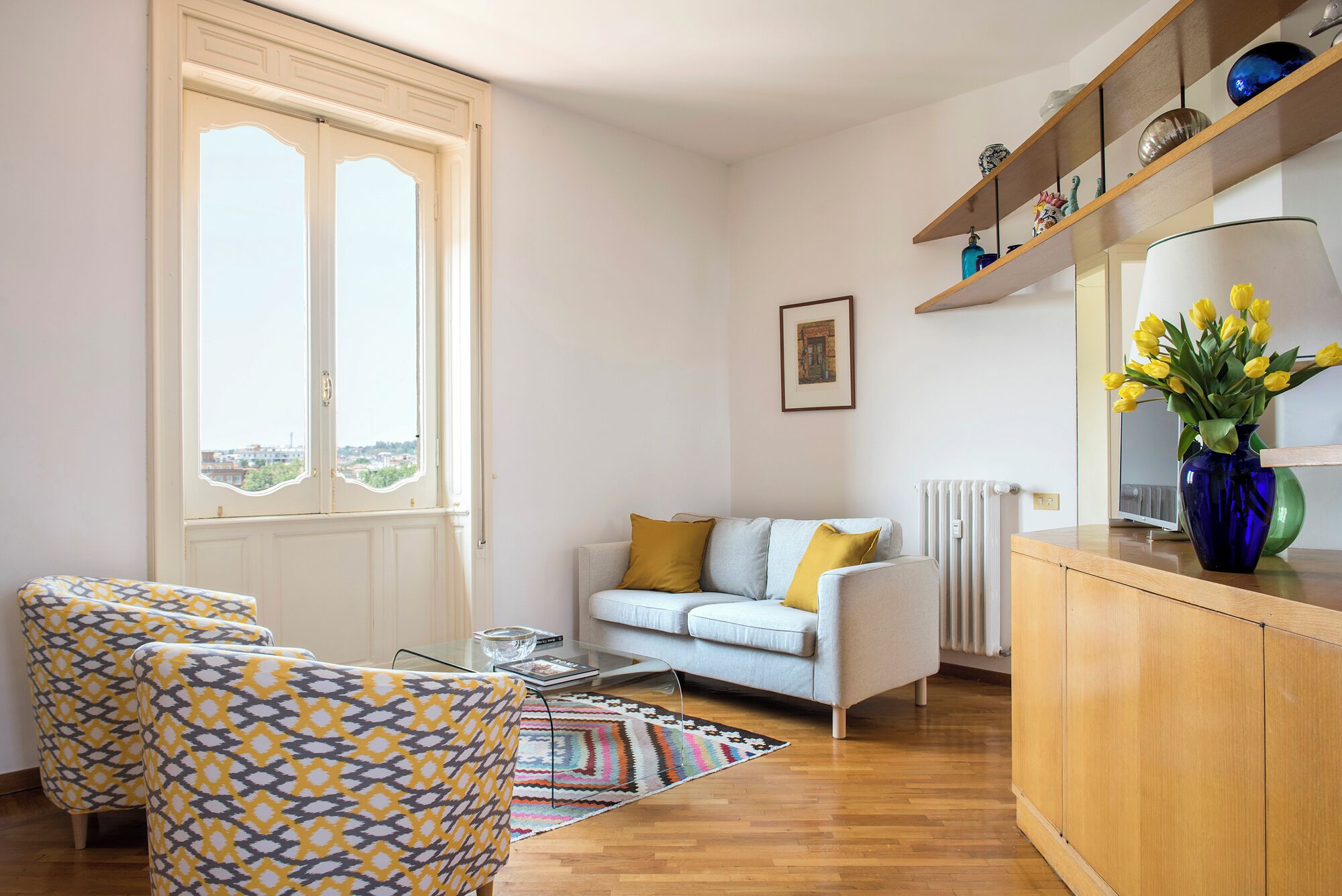 A living room with a sofa, patterned armchairs, a coffee table, and a view through a large window.