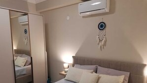 A bedroom with a bed, bedside lamp, air conditioning unit, and a dreamcatcher on the wall.
