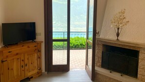 Habitación con televisión sobre un mueble de madera, chimenea y balcón con vistas a zonas verdes y montañas.