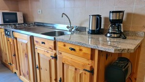 Una cocina con armarios de madera, un lavamanos de acero inoxidable, una cafetera y un tostador.