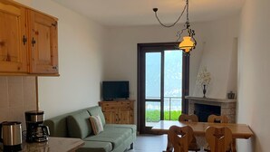Una cocina moderna con armarios de madera, un comedor con mesa y sillas, un sofá verde y un ventanal con vistas a zonas verdes.