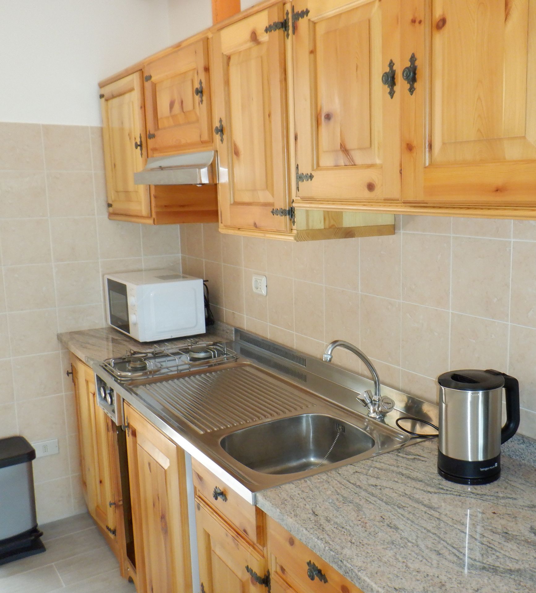 Eine Küche mit Holzausstattung, einem Edelstahlspülbecken, einer Mikrowelle, einem Wasserkocher und einer Kaffeemaschine.