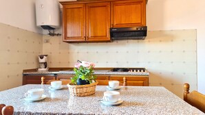 Une cuisine avec des meubles en bois, une cuisinière à gaz, une machine à café et une table mise avec des tasses et un panier de fleurs.
