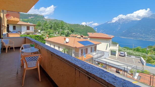 Un balcon aménagé avec du mobilier d’extérieur, une vue sur un lac et des bâtiments en arrière-plan.