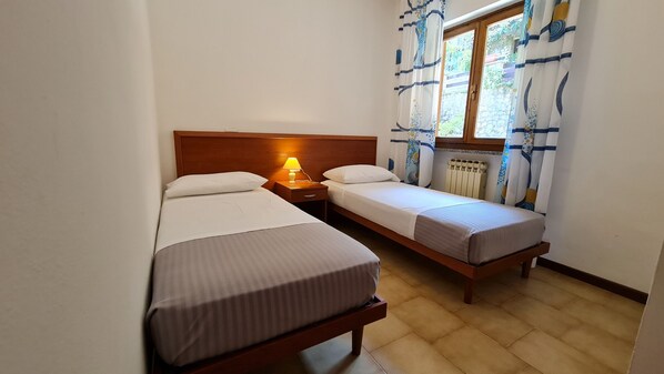 A small, clean room with two single beds, a nightstand with a lamp, and a window with curtains. - Casa Bellicini appartamento Balcony Lake View Park (Tremosine)