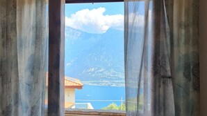 Une pièce avec vue sur les montagnes et un plan d’eau, visible à travers une fenêtre ornée de rideaux.