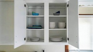 Un mueble blanco con puertas abiertas que muestra estantes con cuencos, platos y tazas.