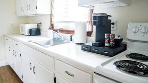 Una cocina con gabinetes blancos, estufa, cafetera y pileta.