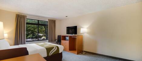 A hotel room with a bed, desk, TV, and a window with curtains.