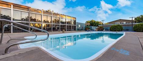 A swimming pool with a metal ladder, surrounded by a concrete deck.