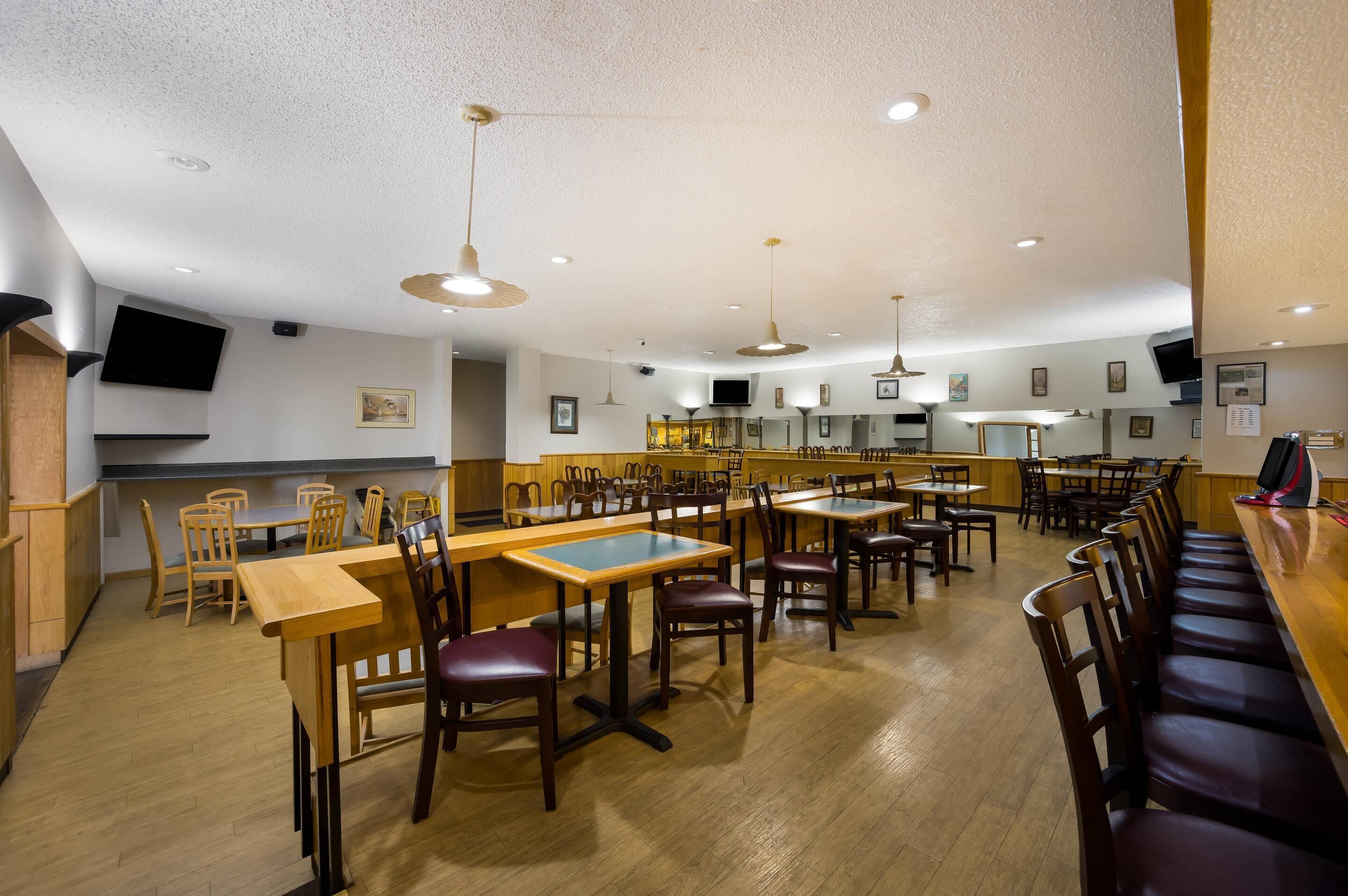 A restaurant with wooden tables and chairs, a bar area, and ceiling lights.