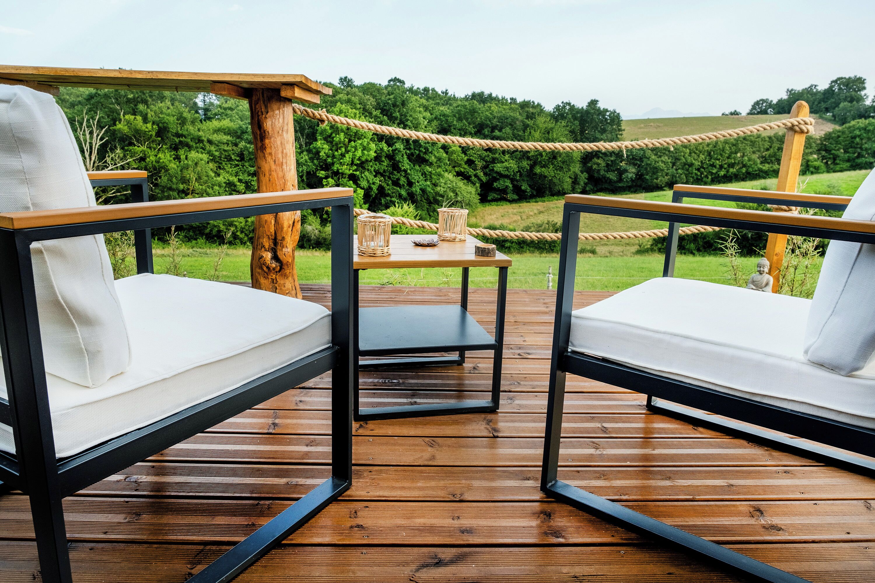 A wooden deck with two white cushioned chairs and a small table with wicker baskets.