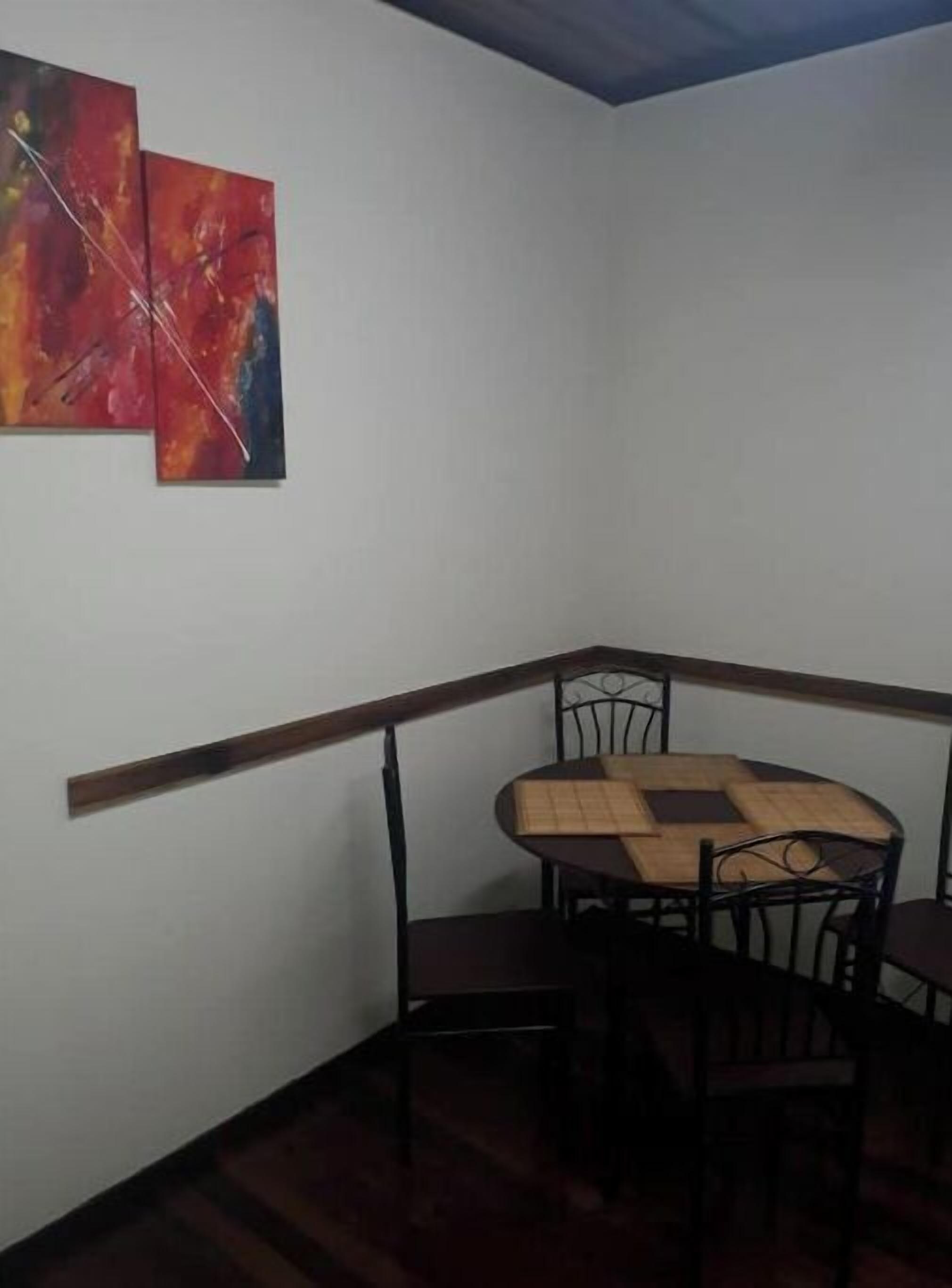 Une pièce d’angle avec une table et des chaises en bois, un mur blanc et deux tableaux abstraits.