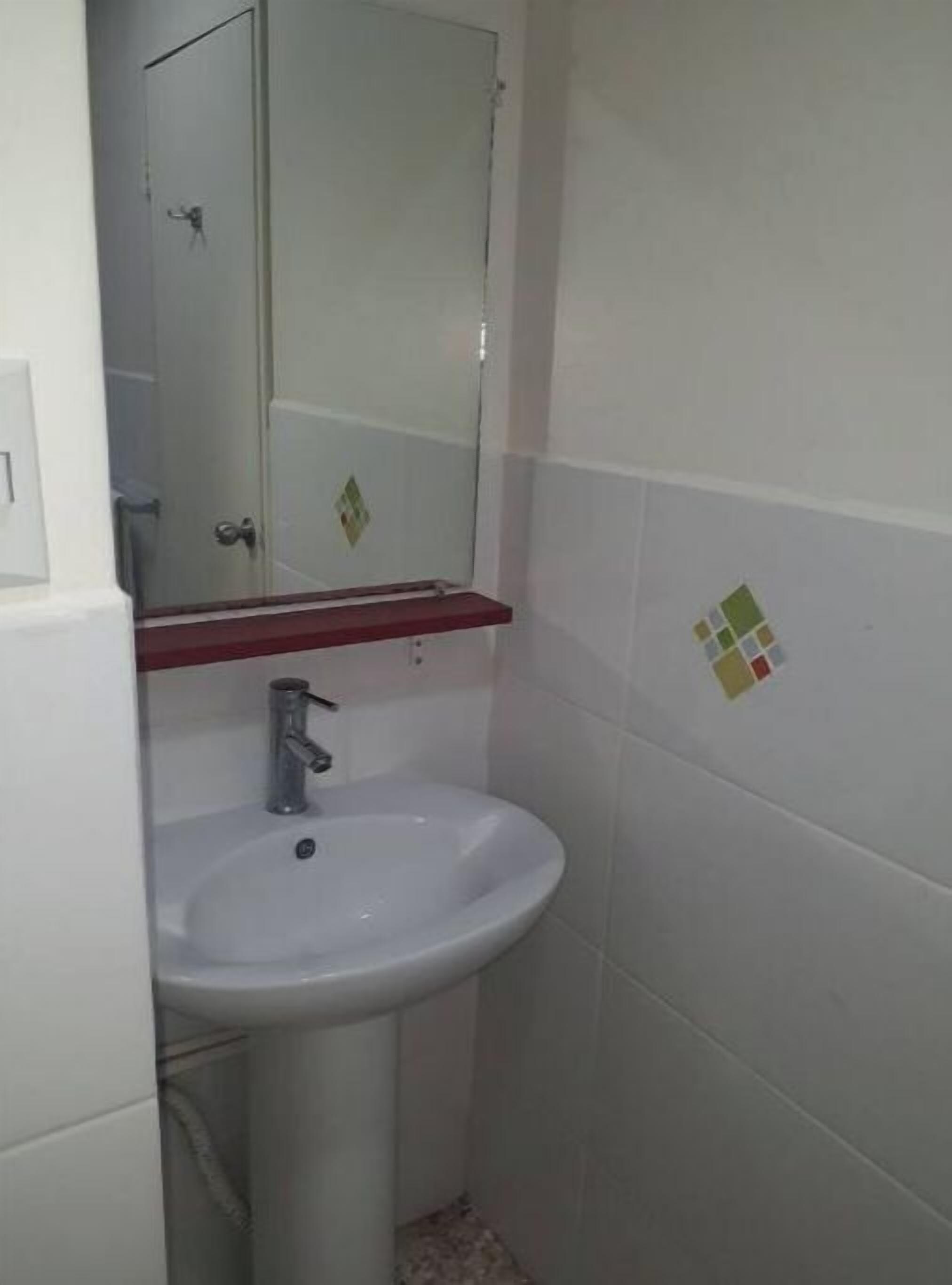 A bathroom with a white sink, a mirror above it, and a red shelf.