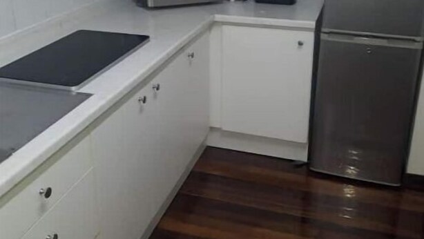 Una cocina compacta con armarios blancos, un microondas, una licuadora y un refrigerador.